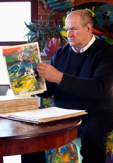 A man seated at a table, examining a painting displayed on its surface.