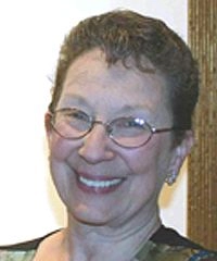 A woman wearing glasses and a black and white shirt, smiling and looking directly at the camera.