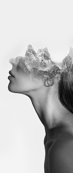 A woman gazes upward with mountains in the background, embodying a sense of wonder and connection to nature.
