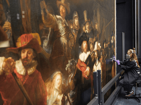 Museum conservator cleaning the surface of Rembrandt's The Night Watch during a restoration project at the Rijksmuseum.